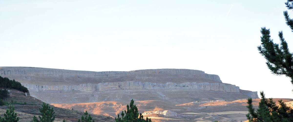 A flat-topped mesa with sparse vegetation and a clear sky.