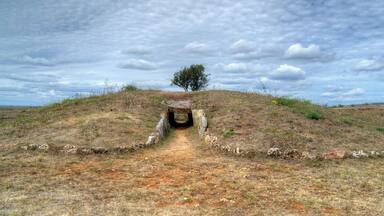 A dry, grassy hill with a stone structure at the top and a narrow path leading to it.