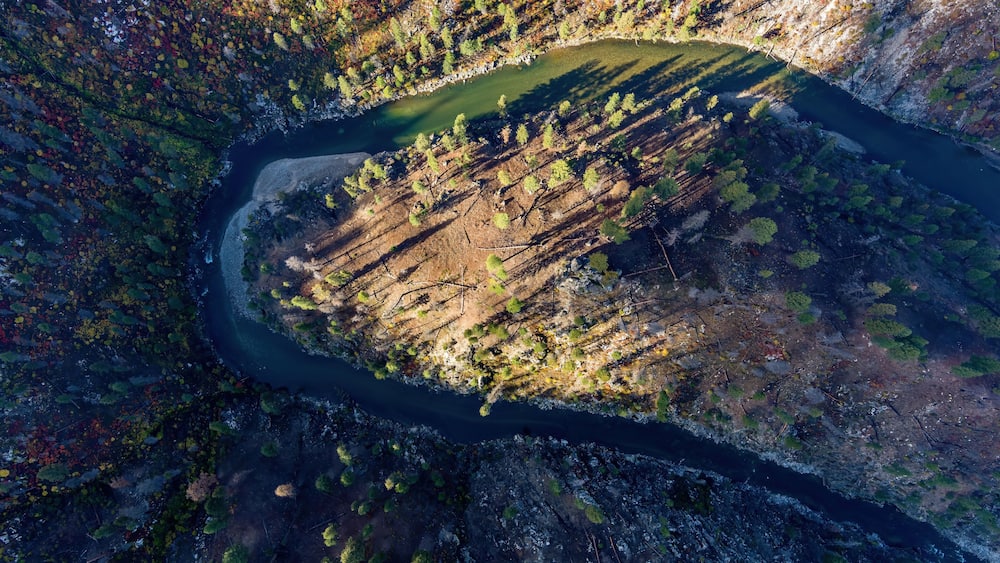 An aerial view of a river winding through a forested valley with a small lake.