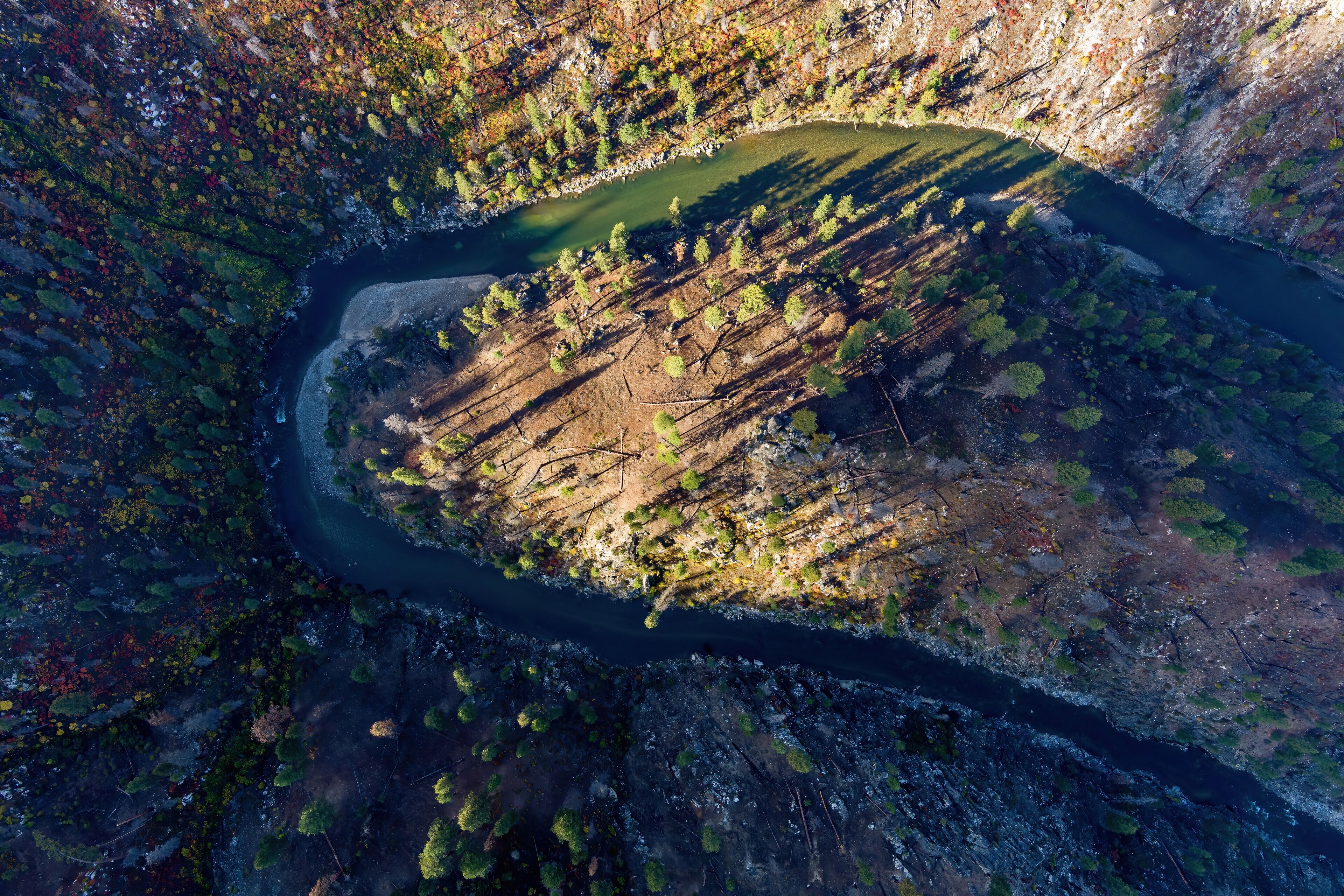 An aerial view of a river winding through a forested valley with a small lake.