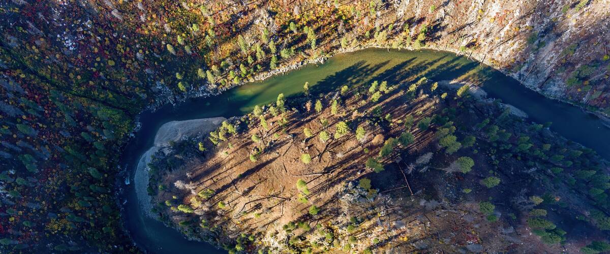 An aerial view of a river winding through a forested valley with a small lake.