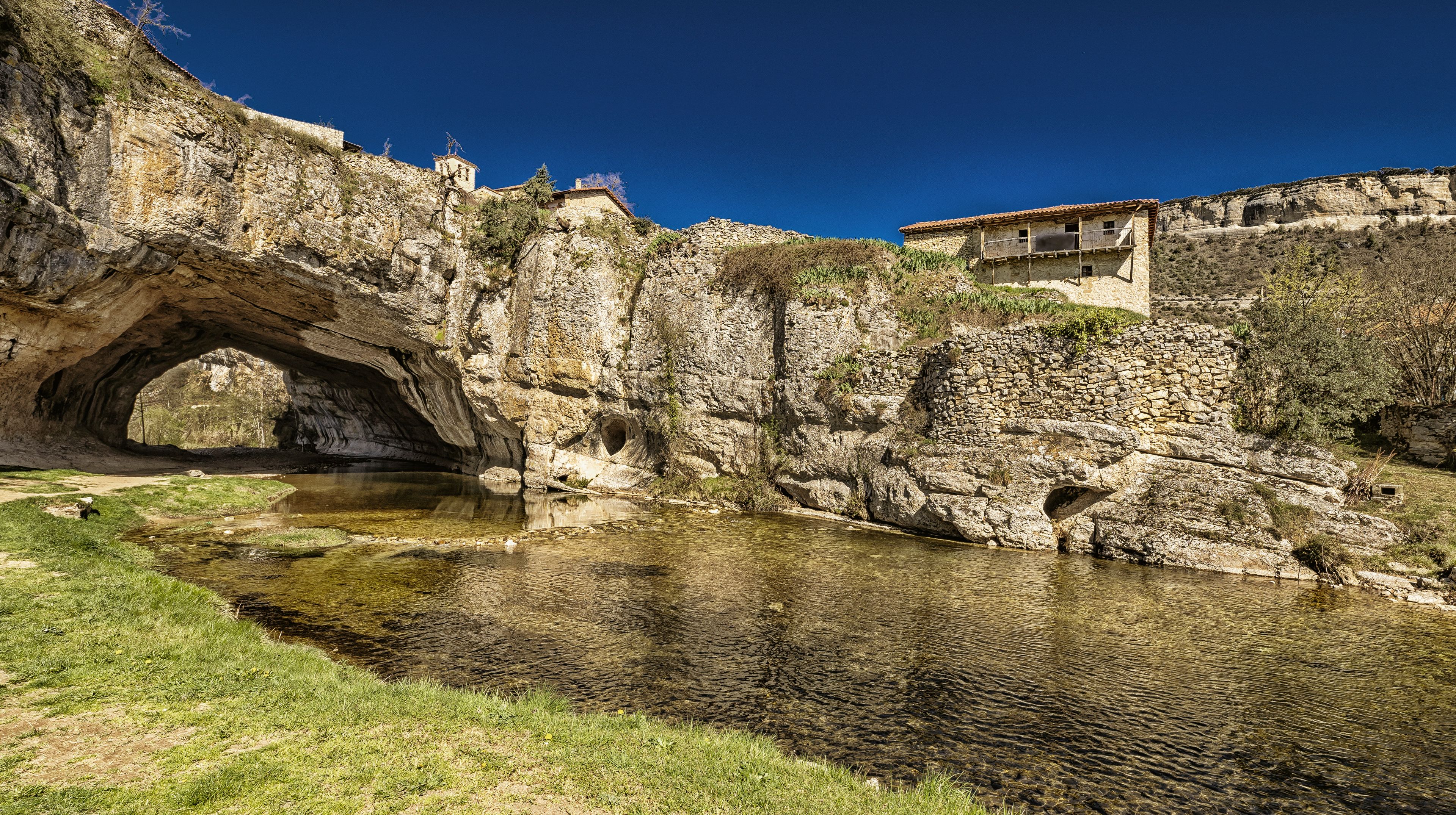 A stone bridge over a river, surrounded by rocky cliffs and a small building.