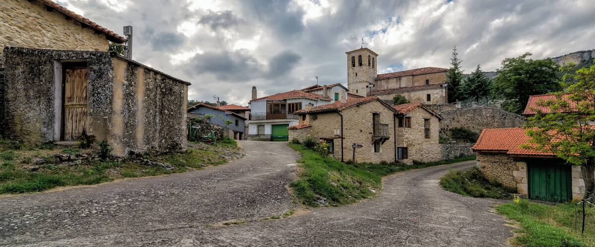 A cobblestone street in a historic village with stone buildings and a church tower.