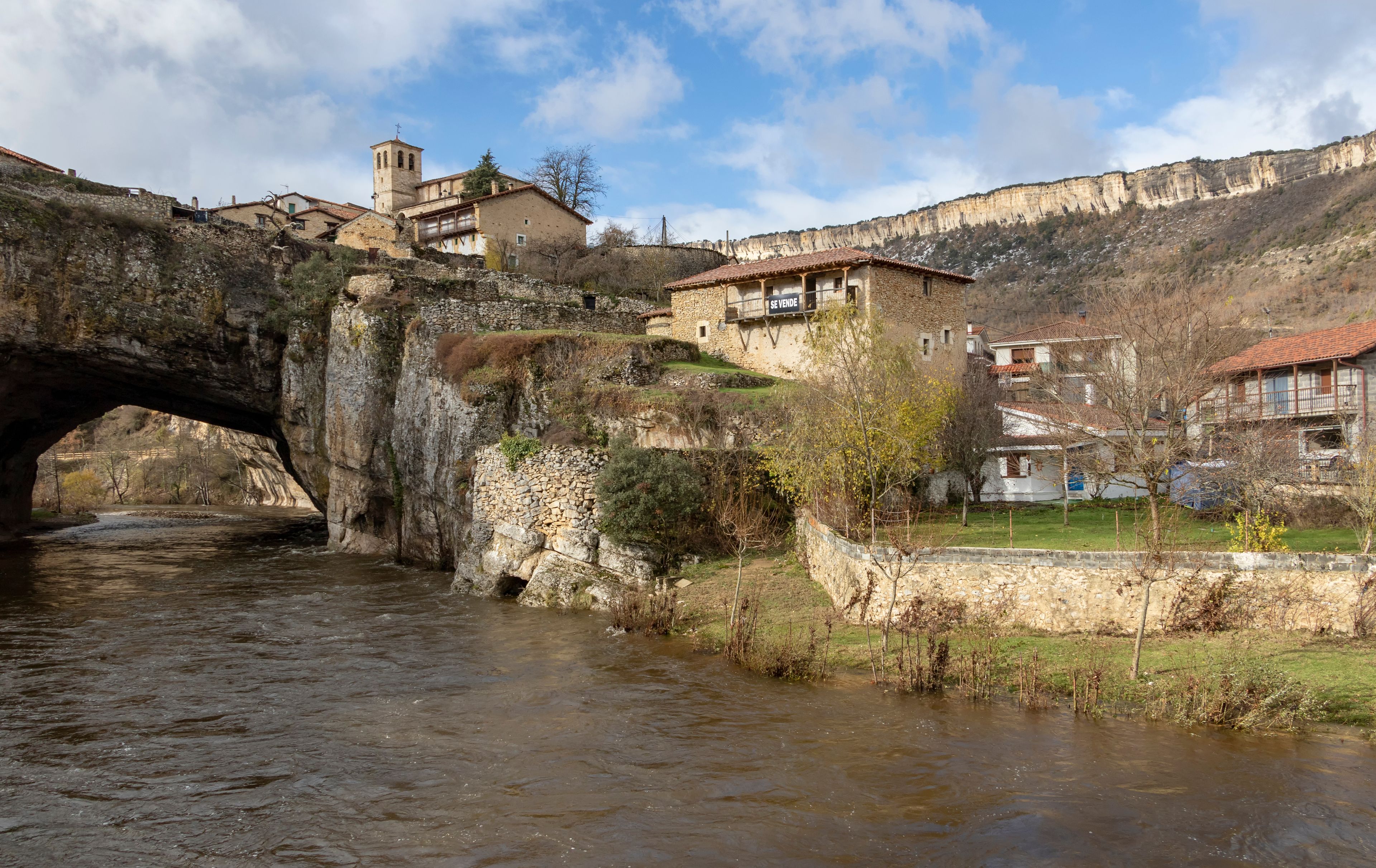 A stone bridge over a river, a historic building with a bell tower, and a mountainous backdrop.