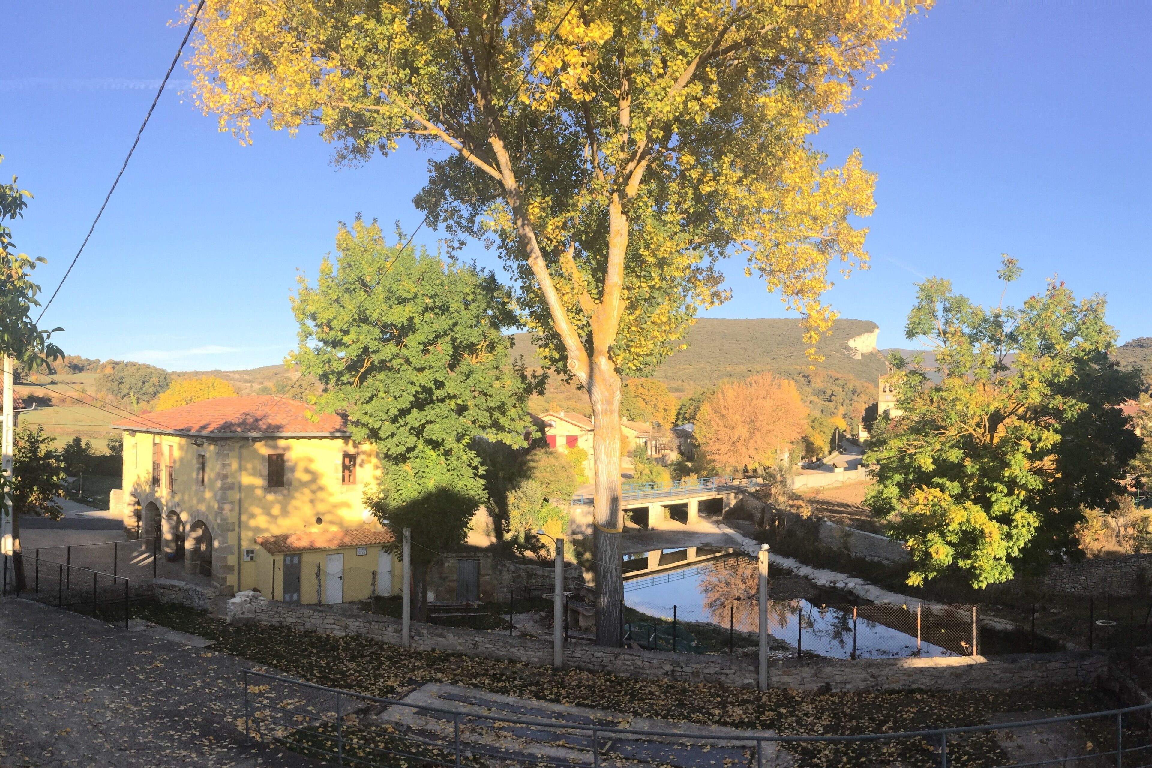 Escuela porticada, Bolera tres tablones, charca en el lecho de rio Trema, Iglesia de San Juan y Montes de la Rad y la Isa con el Somo al fondo