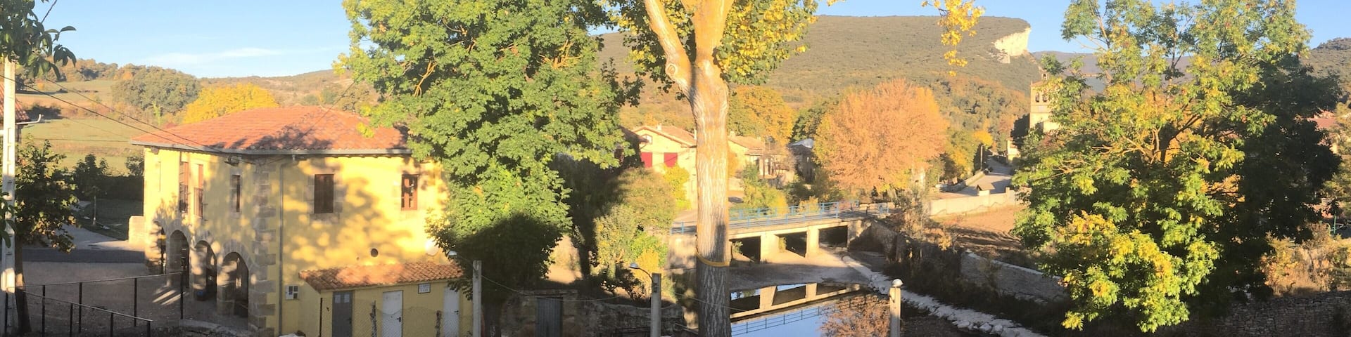 A rural landscape with a river, a bridge, and a building with a red roof.