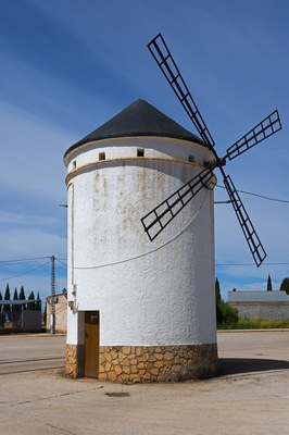 A windmill with a white facade and a stone base, set against a clear blue sky.