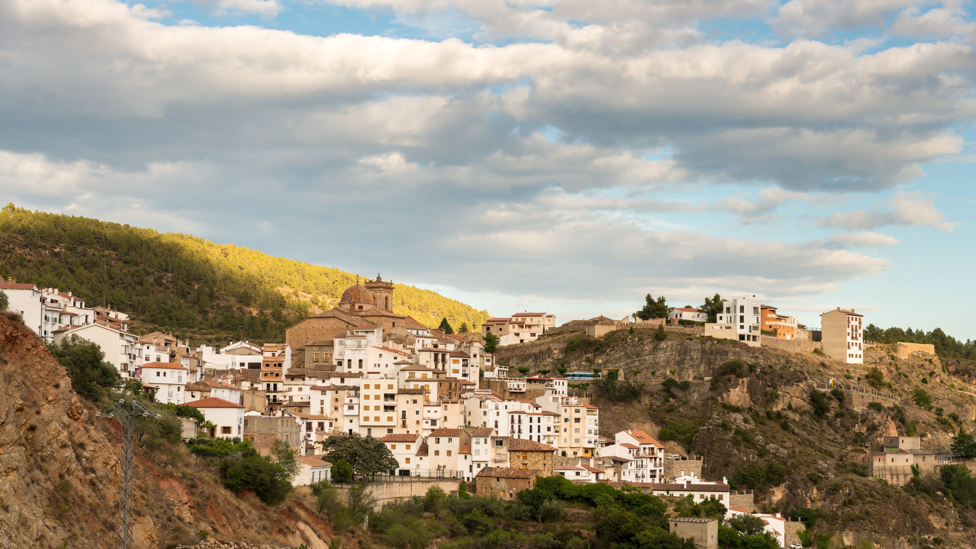 A hillside town with white buildings, a prominent church, and a rocky hill in the background.