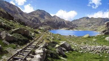 Un paisaje montañoso con una vía de tren, un lago y terreno rocoso.