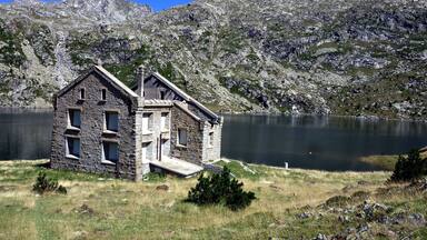 A stone house by a lake with mountains in the background.