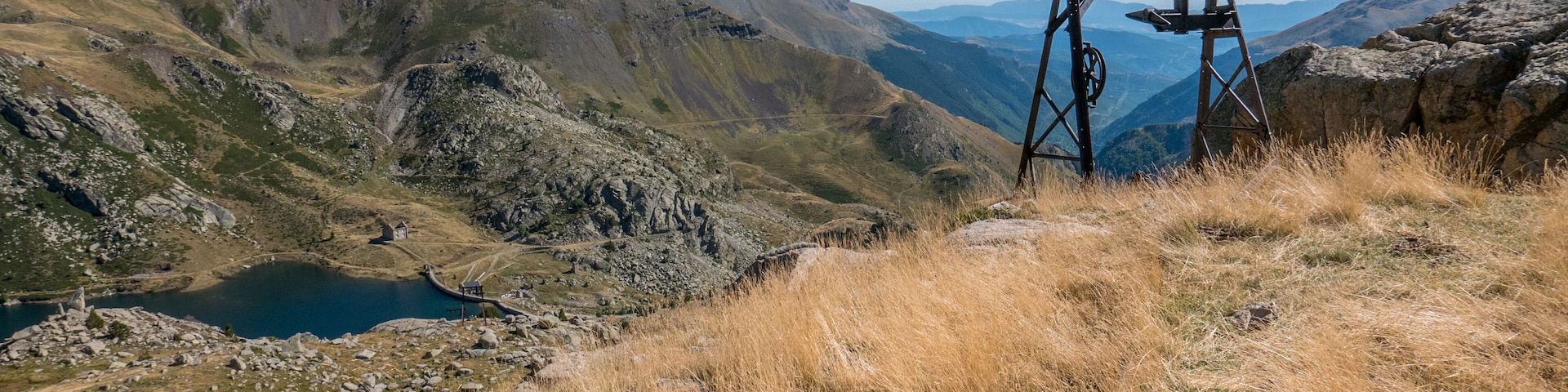 Paisagem montanhosa com um lago, terreno rochoso e uma estrutura de madeira em primeiro plano.