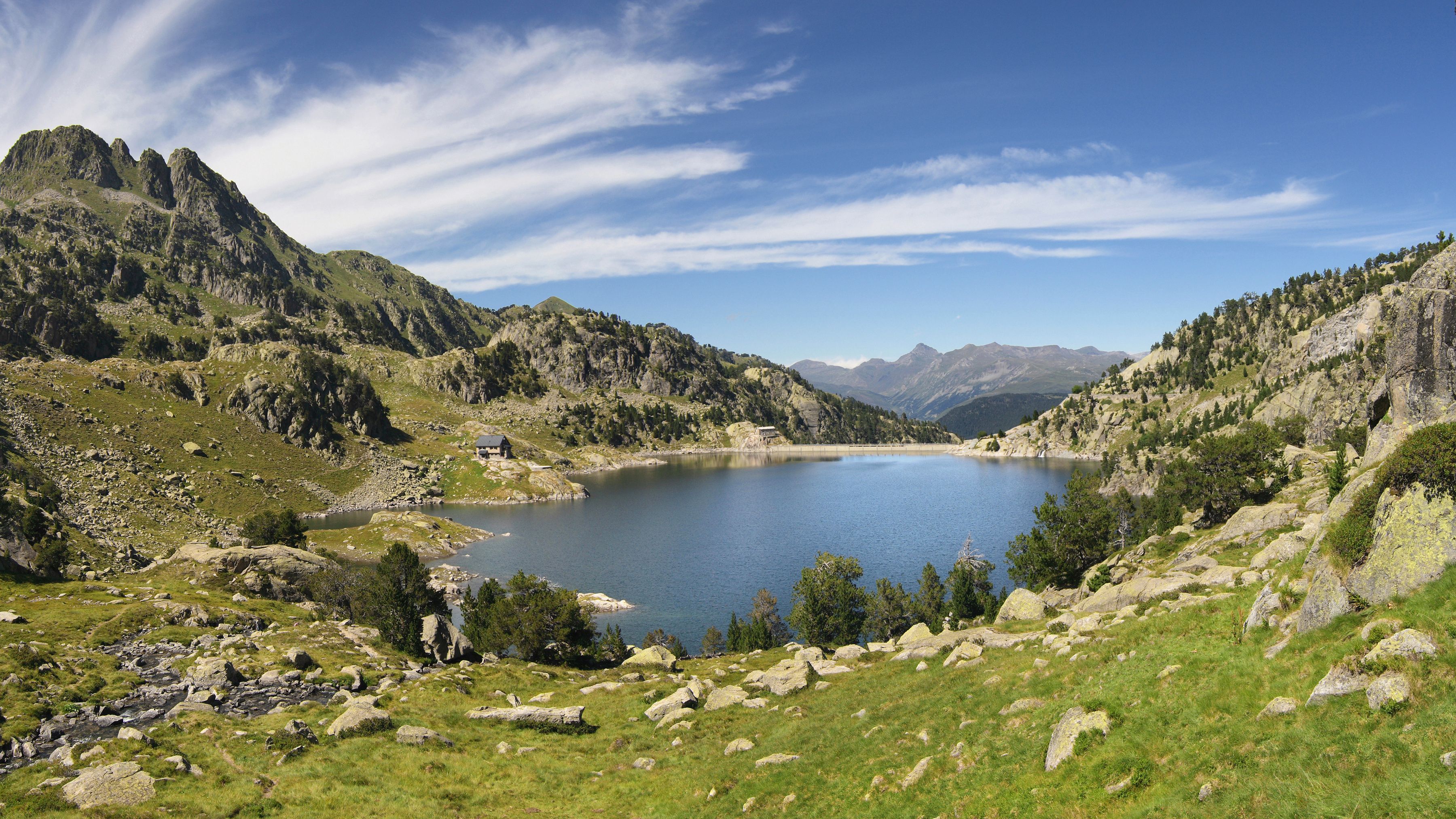 A mountainous landscape with a lake, rocky terrain, and a small cabin.