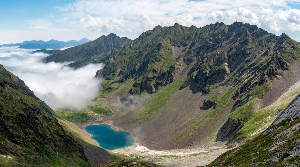 A mountainous landscape with a turquoise lake surrounded by rugged peaks and clouds.