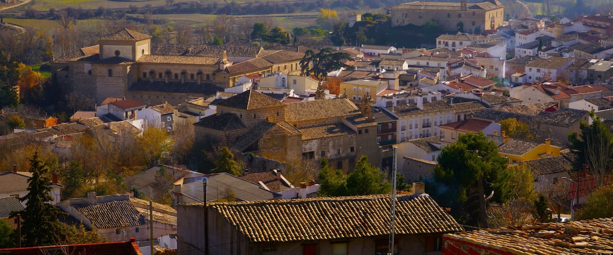 A town with historic buildings, rolling hills, and a river in the background.