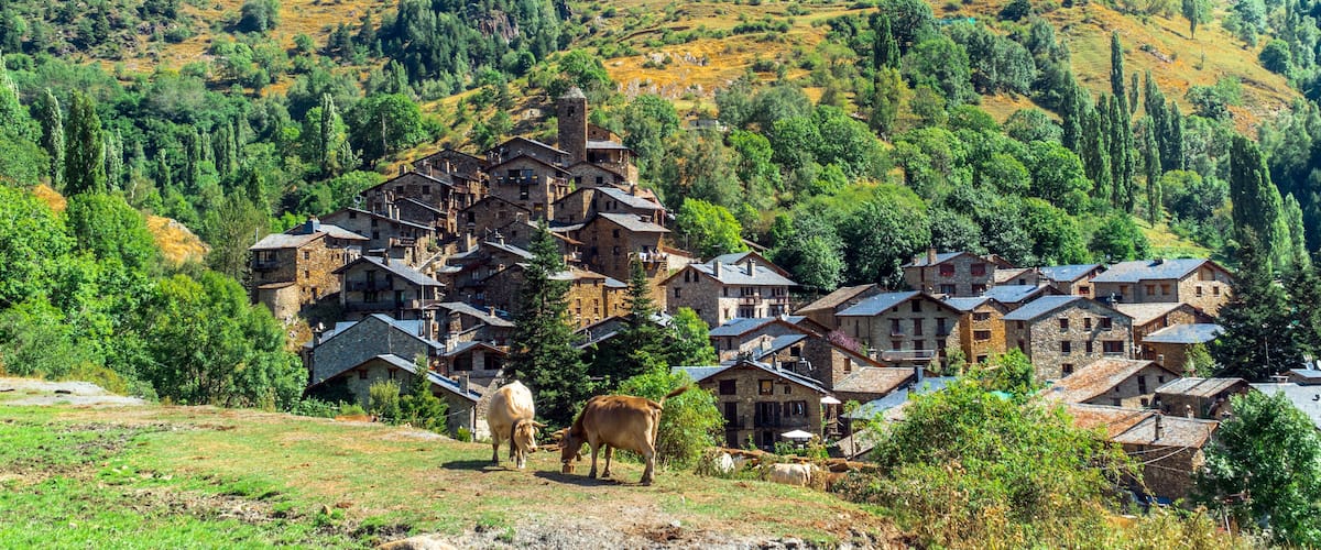 A village with stone buildings nestled in a hilly, forested landscape.