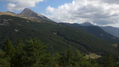 Paisagem montanhosa com florestas densas e um pico imponente ao longe.