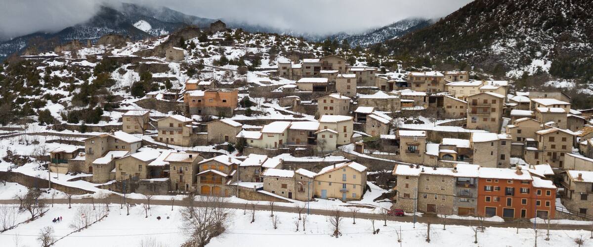 A snow-covered village with stone buildings nestled in a mountainous area.