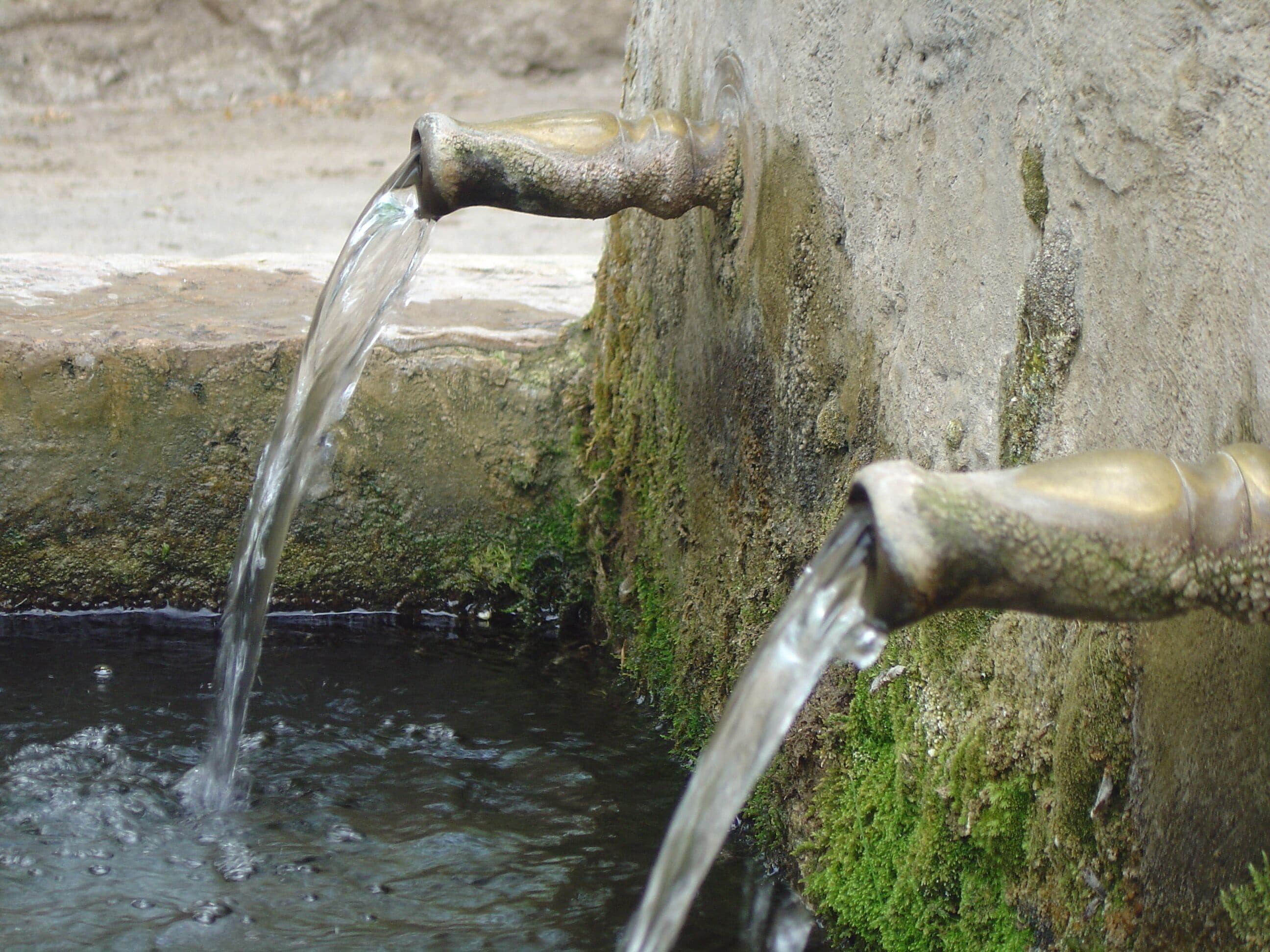 A stone water spout with water flowing into a pool.