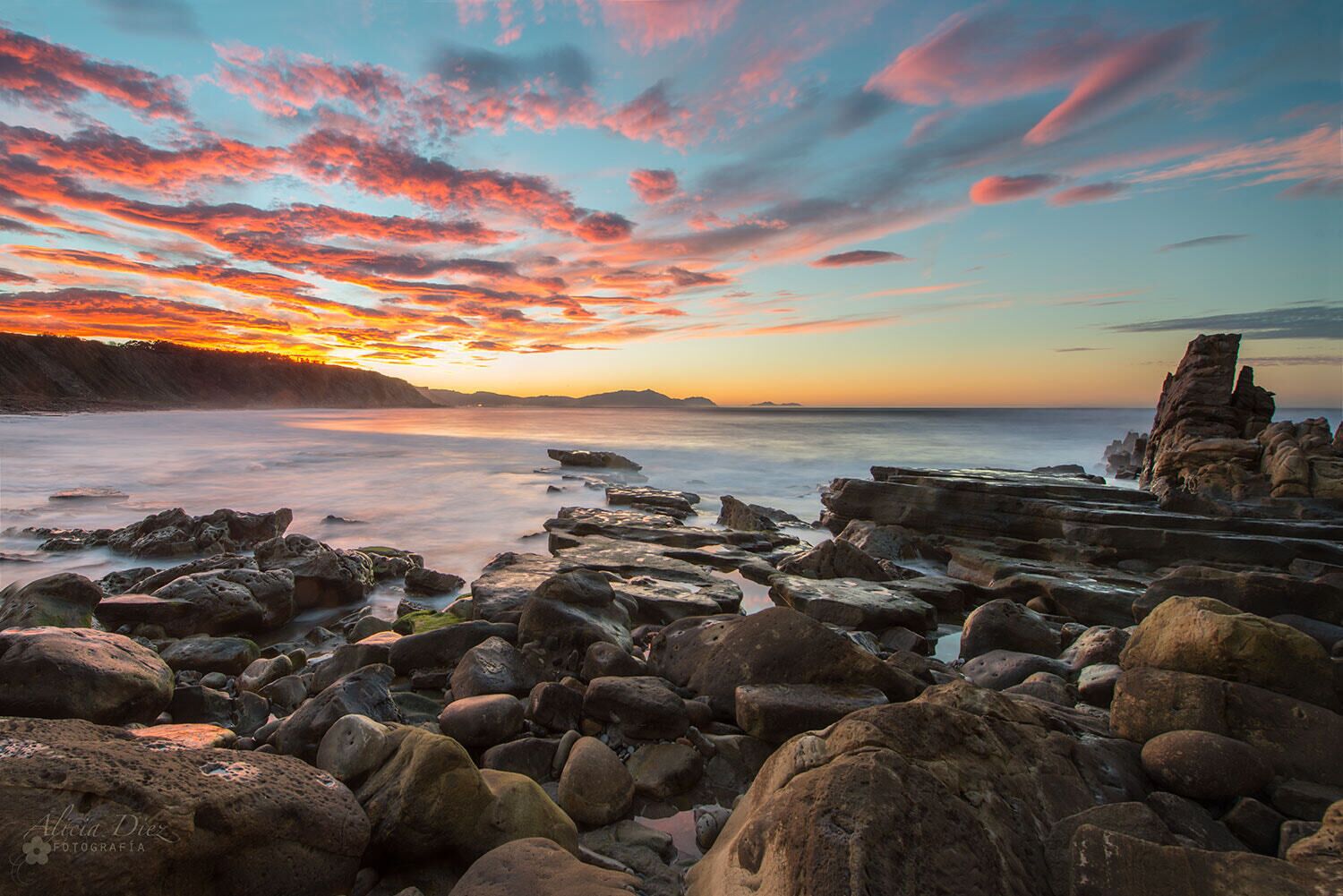 A rocky shoreline with a sunset and a distinctive rock formation.