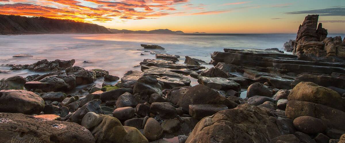 A rocky shoreline with a sunset and a distinctive rock formation.