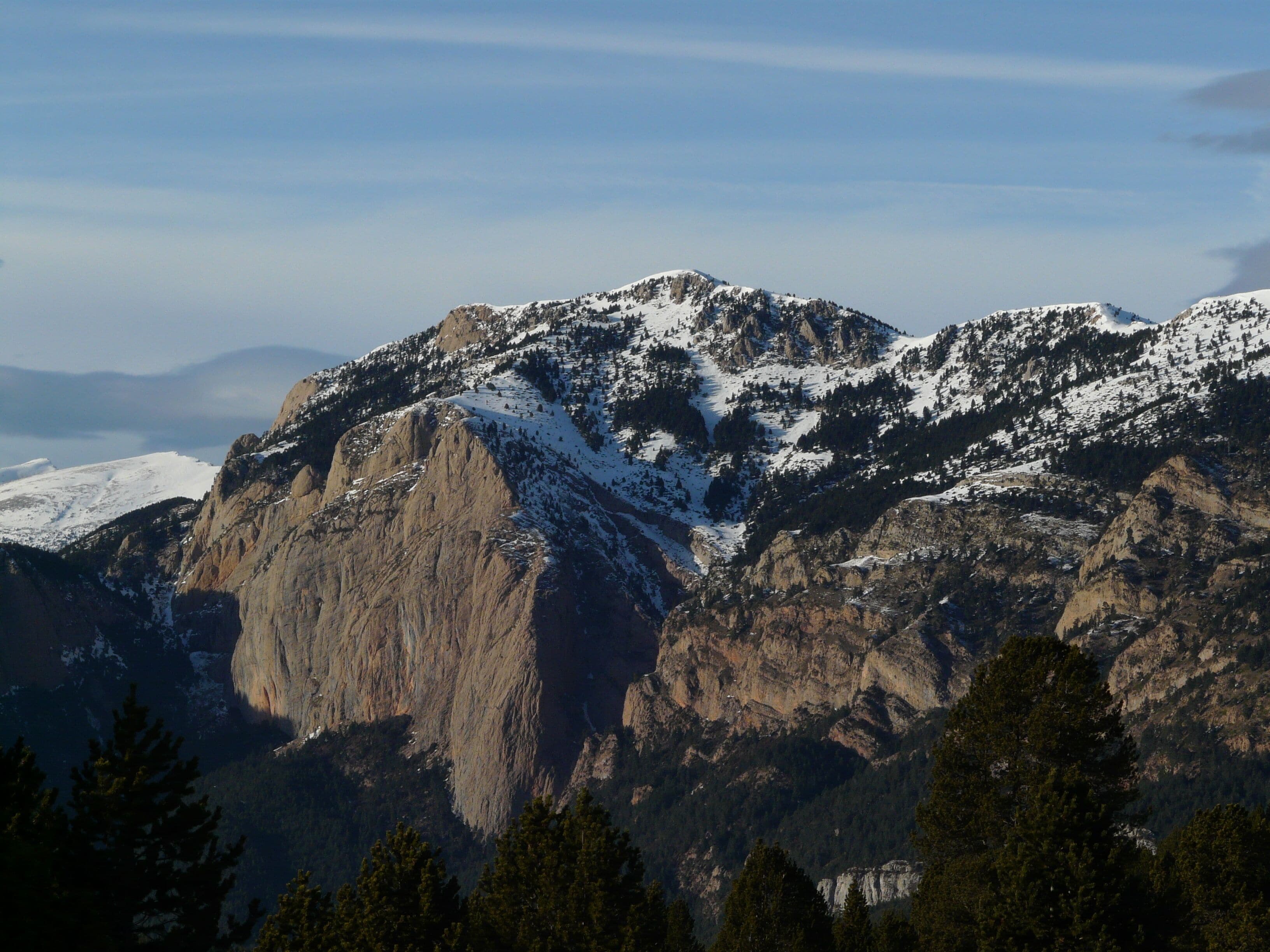 A snow-covered mountain range with rugged peaks and dense forests at the base.