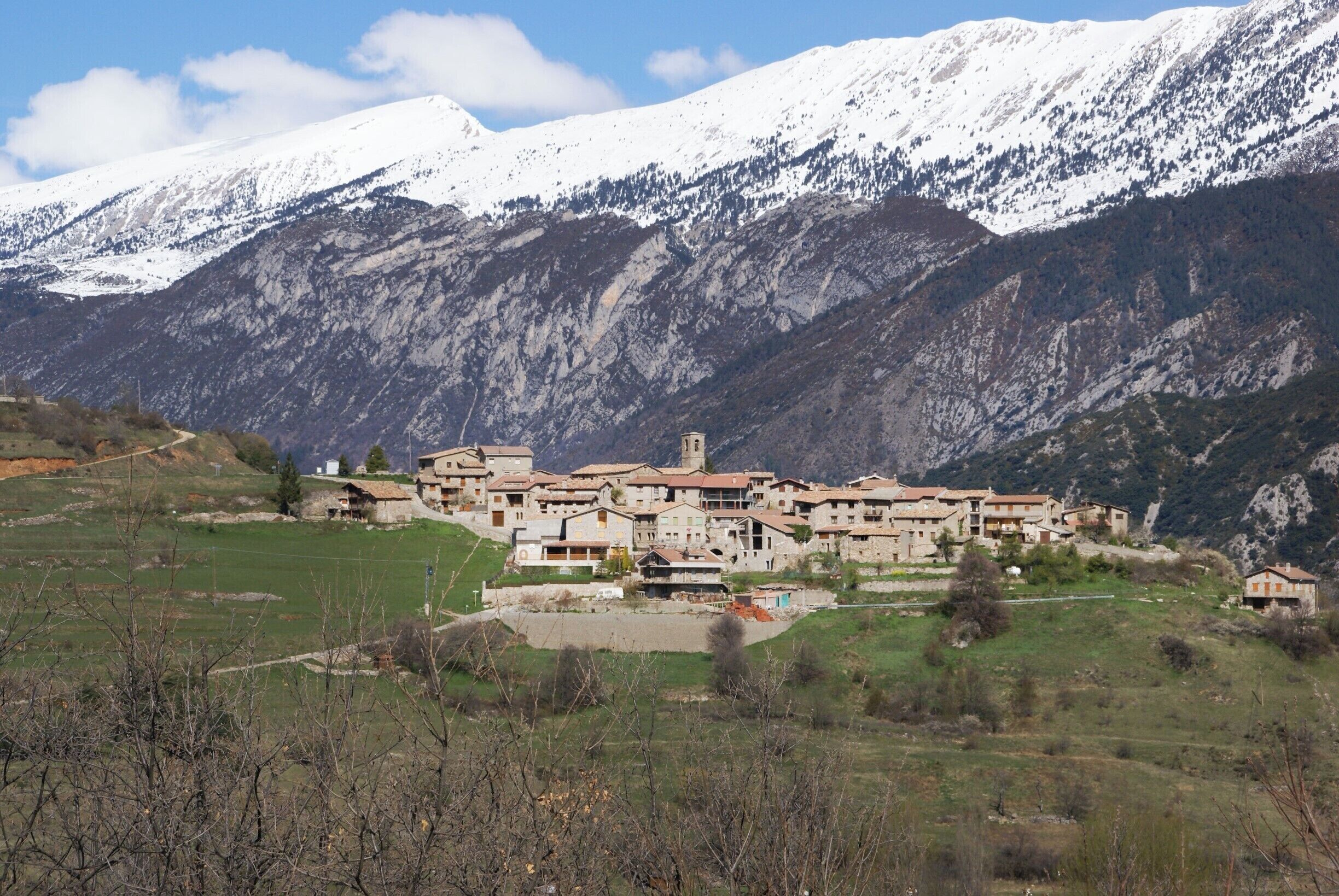 A village with traditional buildings nestled in a valley, surrounded by snow-capped mountains.