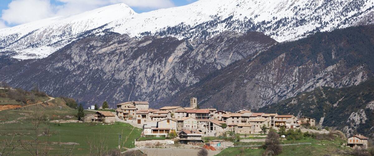 A village with traditional buildings nestled in a valley, surrounded by snow-capped mountains.