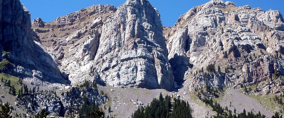 A rugged mountain landscape with prominent rocky peaks and dense forested areas.