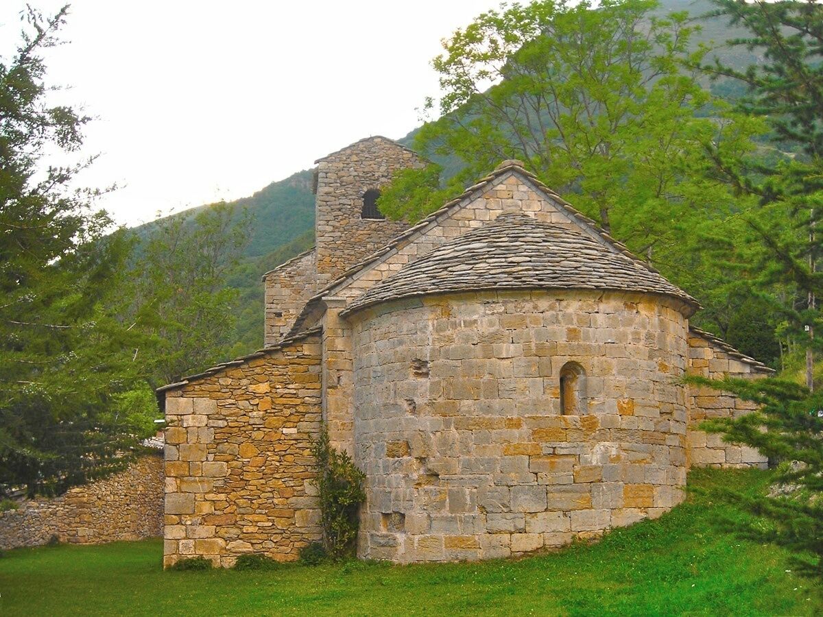 A stone church with a bell tower, surrounded by lush greenery and hills.