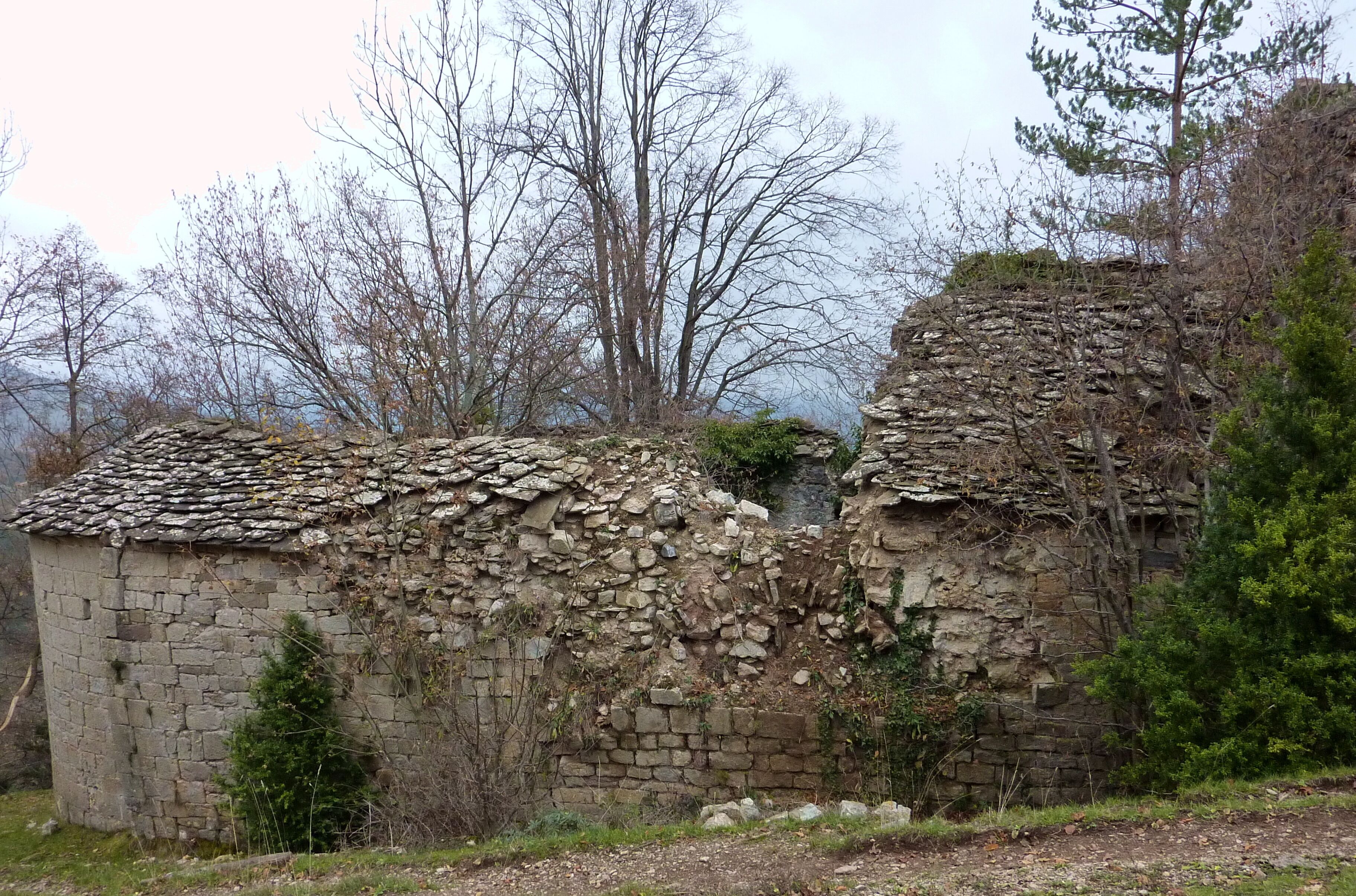 A stone building with a tiled roof, surrounded by trees and vegetation.