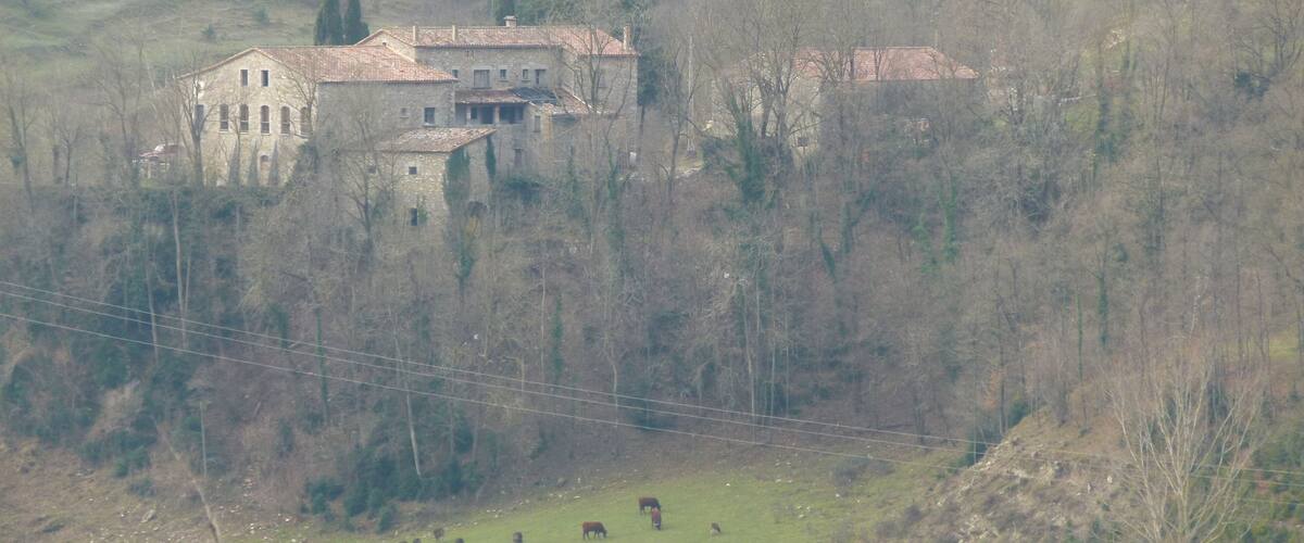 A stone building with a tiled roof surrounded by trees and hills.
