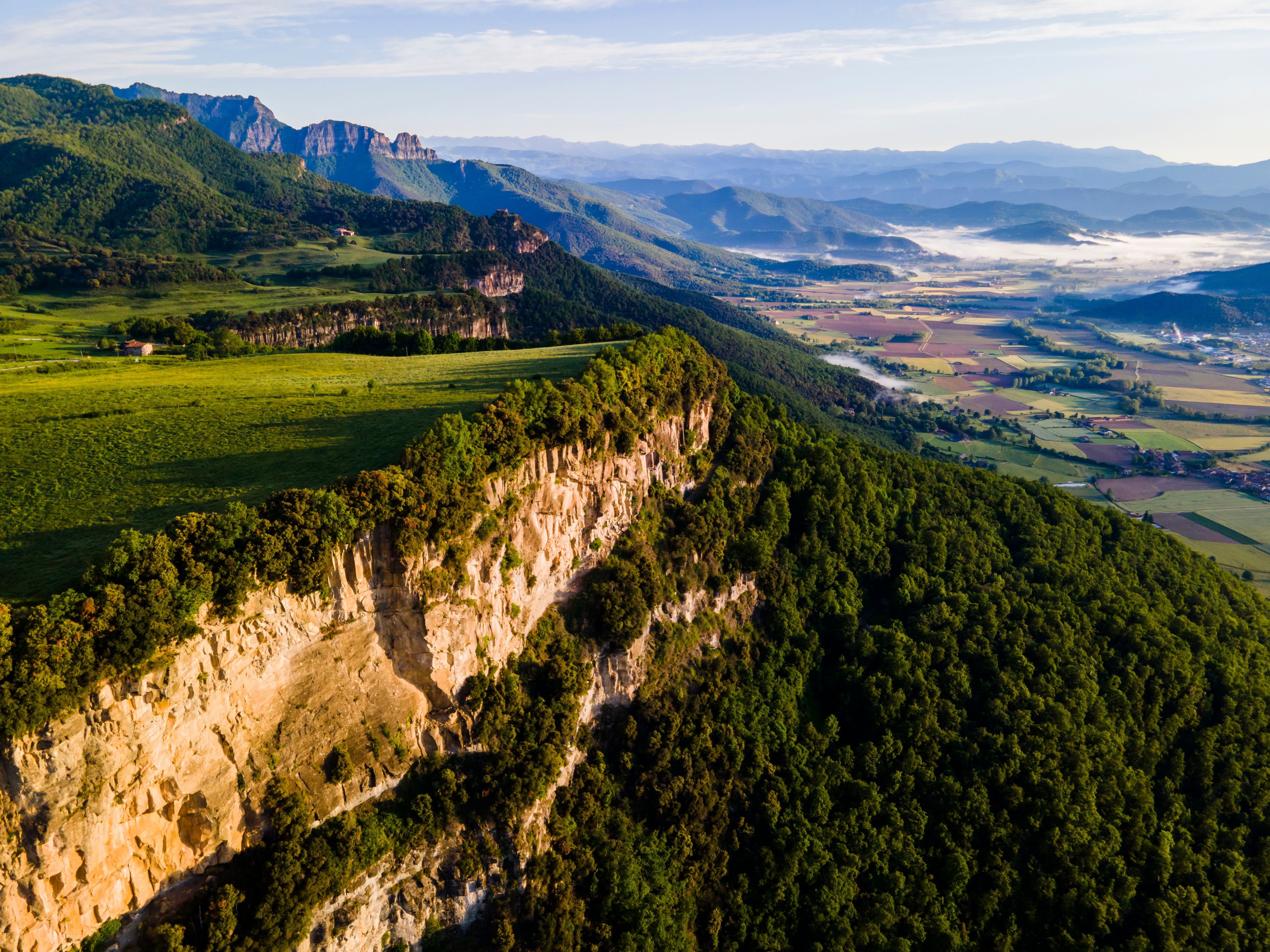 A mountainous landscape with a river valley, cliffs, and scattered buildings.