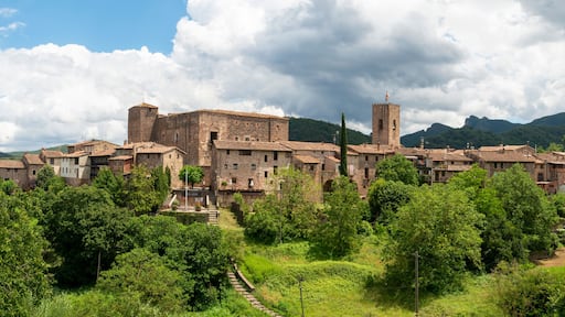 Un pueblo histórico con edificios de piedra, una torre destacada y abundante vegetación.