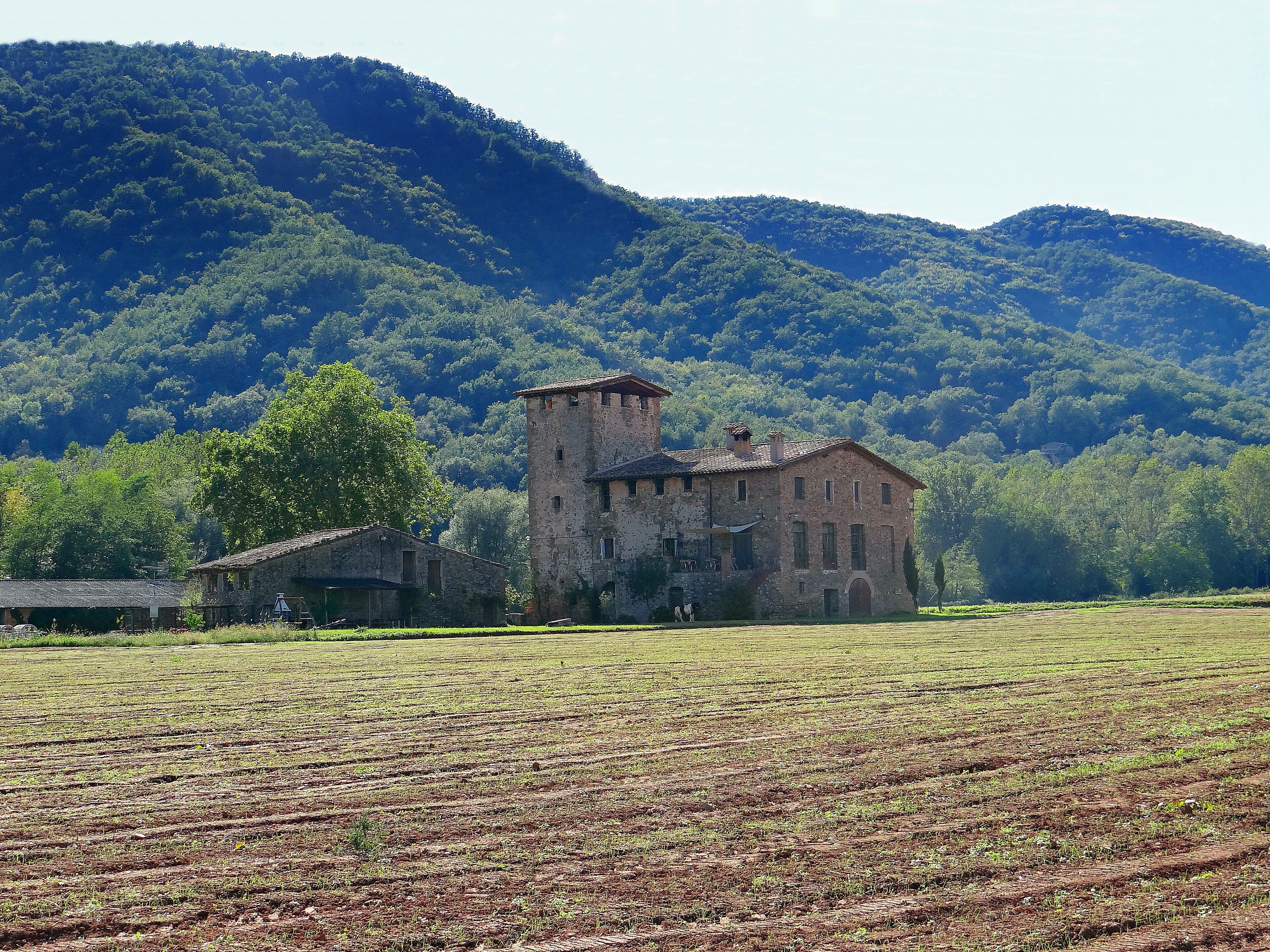 A historic stone building surrounded by a cultivated field and forested hills.