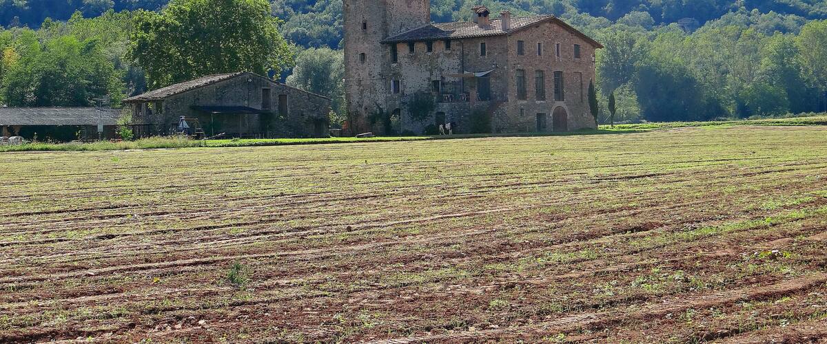 A historic stone building surrounded by a cultivated field and forested hills.