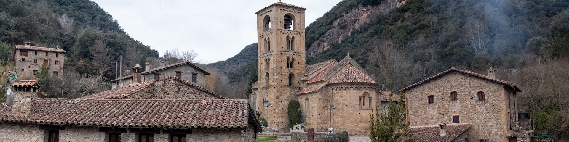 A stone church with a bell tower, surrounded by stone buildings and a mountainous landscape.