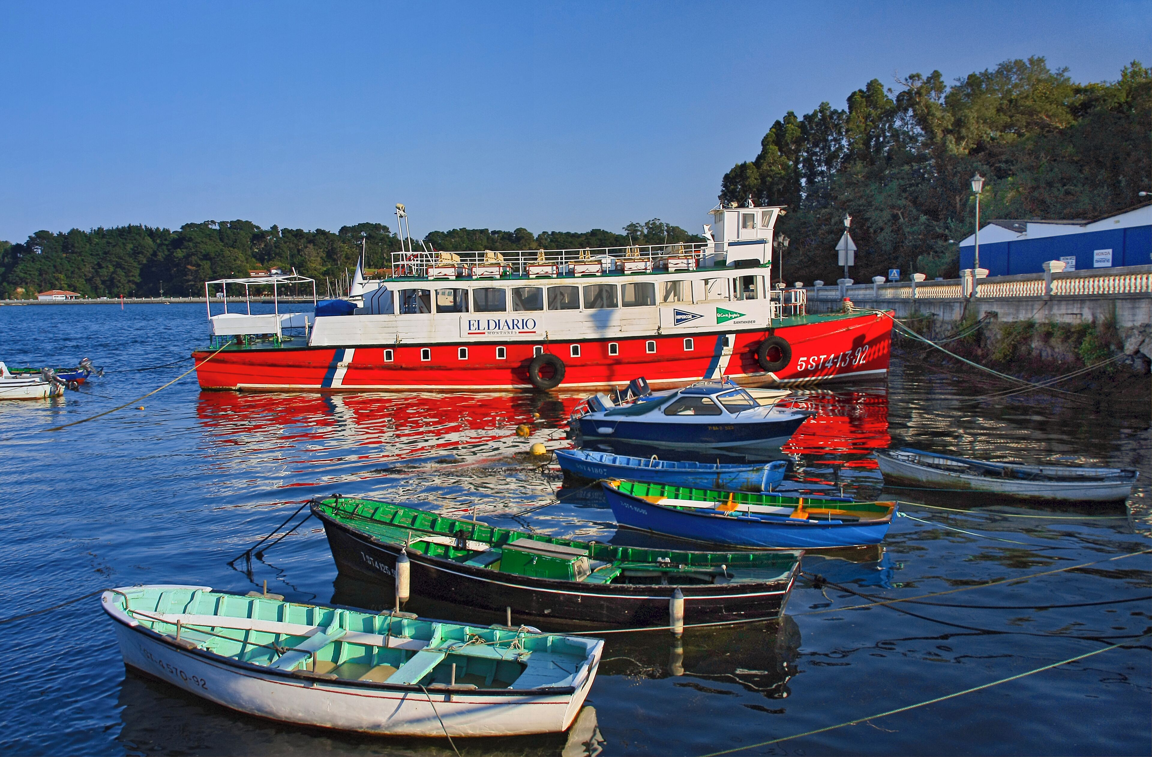 A red and white boat named "EL DIARIO" docked at a harbor with smaller boats around it.