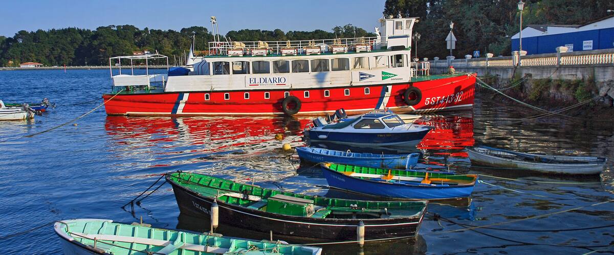 A red and white boat named "EL DIARIO" docked at a harbor with smaller boats around it.