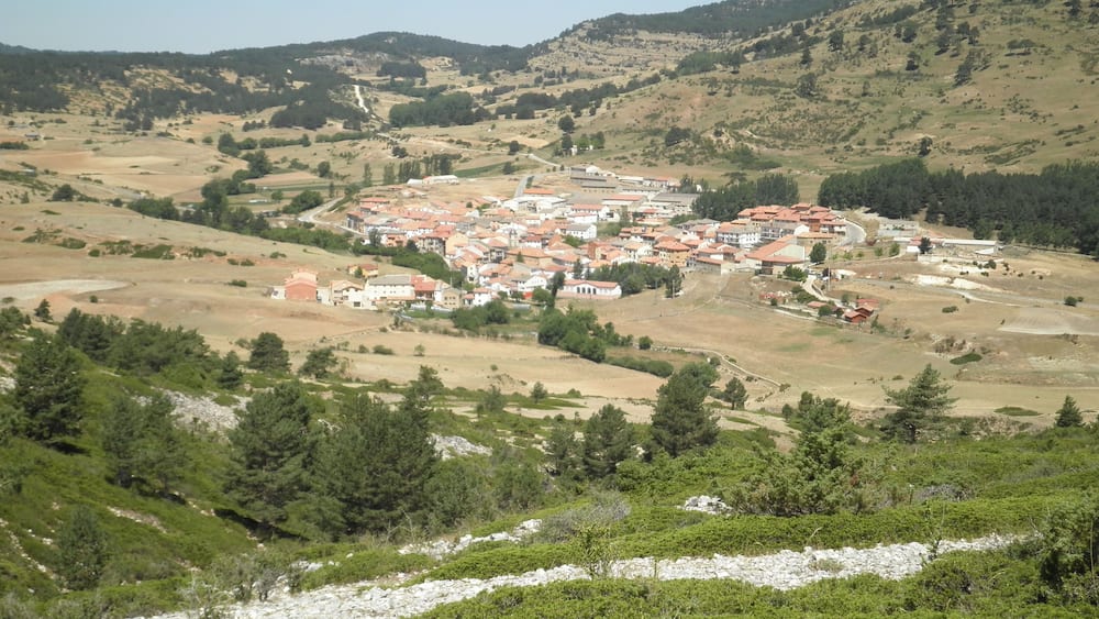 A hillside village with terraced houses and a river in the foreground.