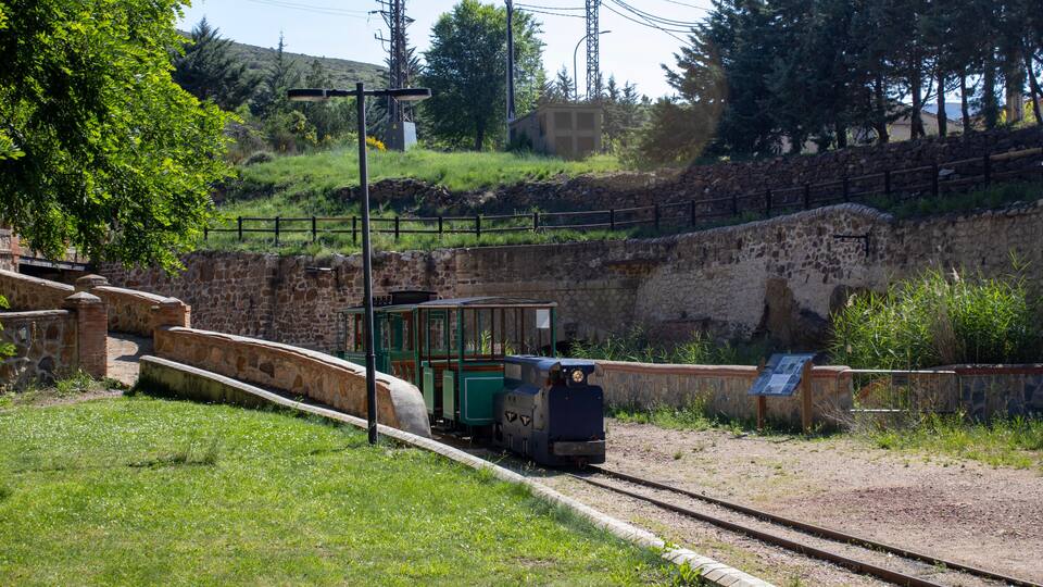 A small train on a track, surrounded by greenery and stone walls.