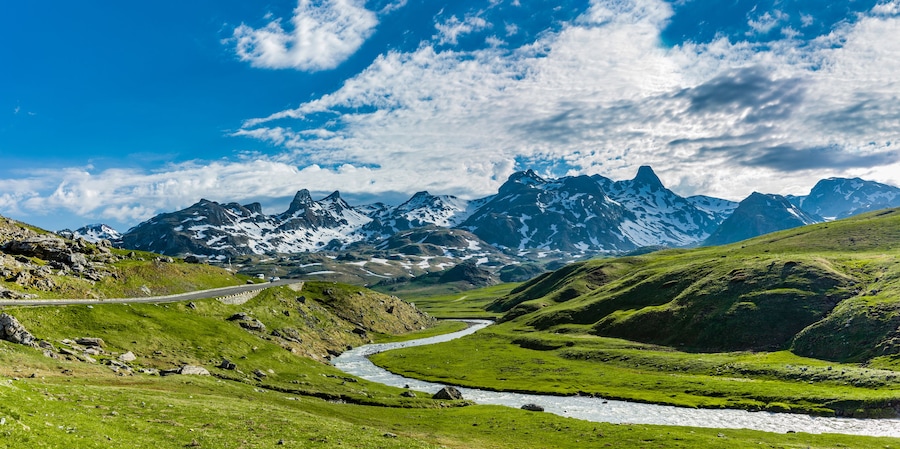 Paisaje montañoso con un río, una carretera y picos nevados.