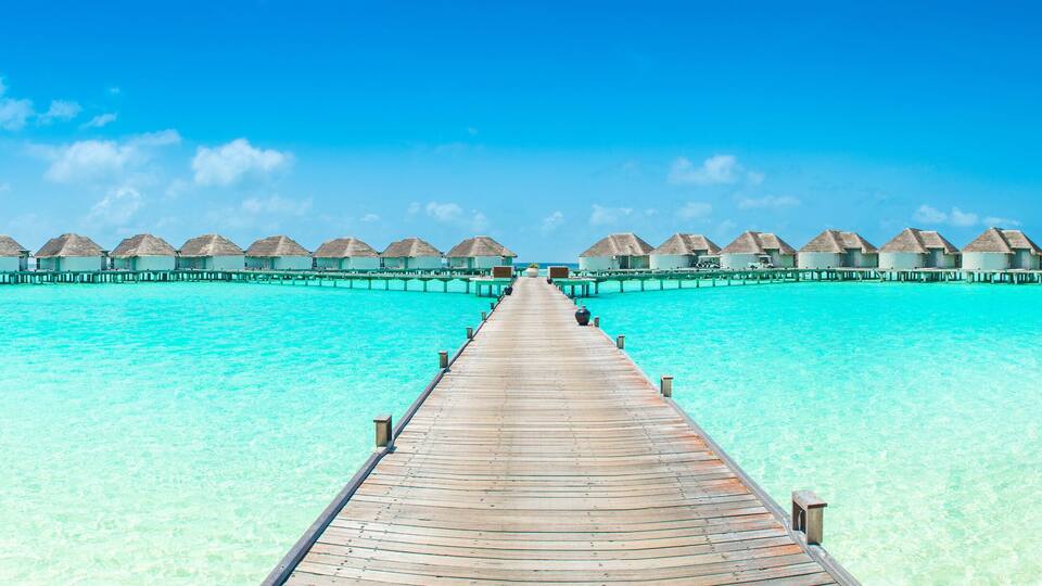 A wooden pier leading to overwater bungalows in clear turquoise waters.