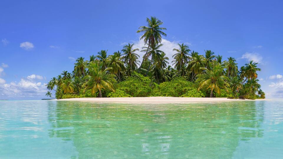 A tropical island surrounded by clear turquoise waters and a clear blue sky.