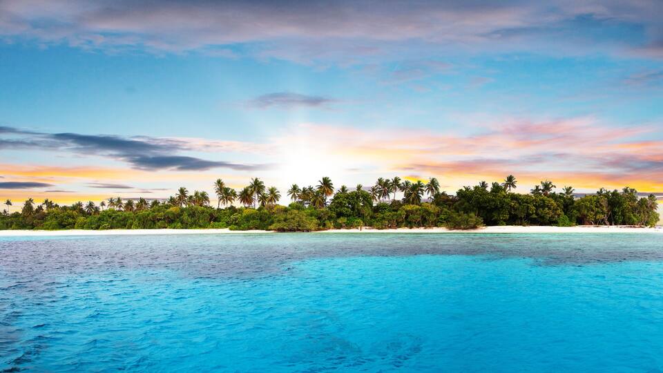 A tropical island with clear turquoise waters and a sunset sky.