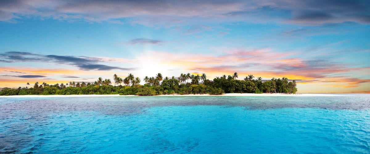 A tropical island with clear turquoise waters and a sunset sky.