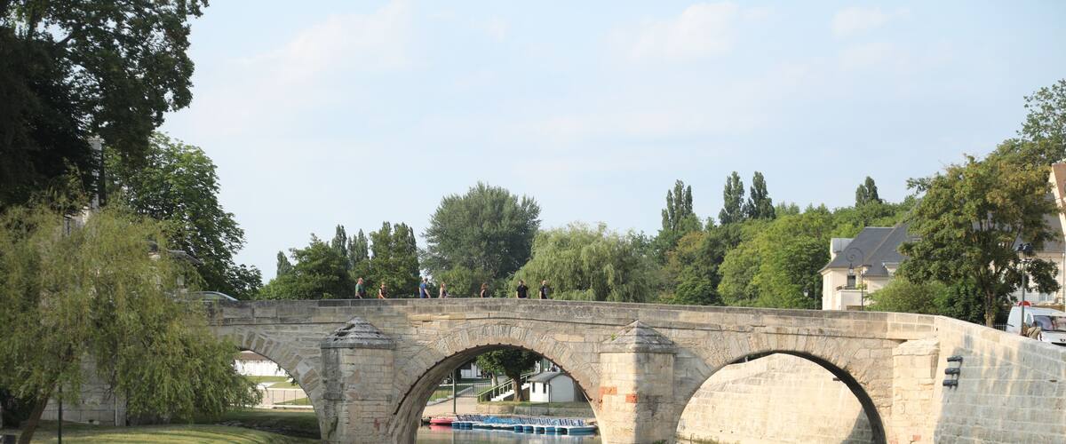 A stone bridge over a calm river with a swan swimming below.