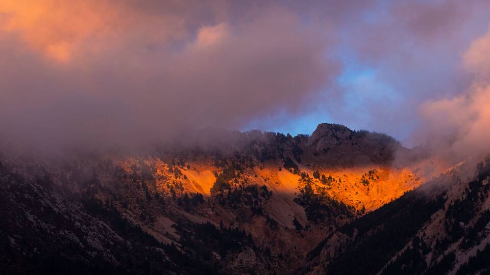 A mountain range with a valley illuminated by sunlight, surrounded by clouds.