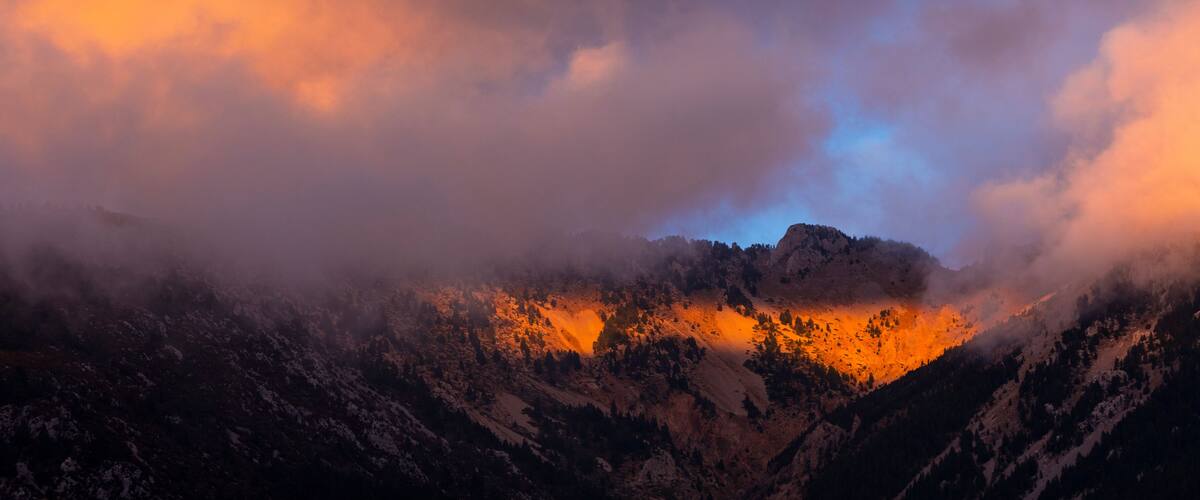 A mountain range with a valley illuminated by sunlight, surrounded by clouds.