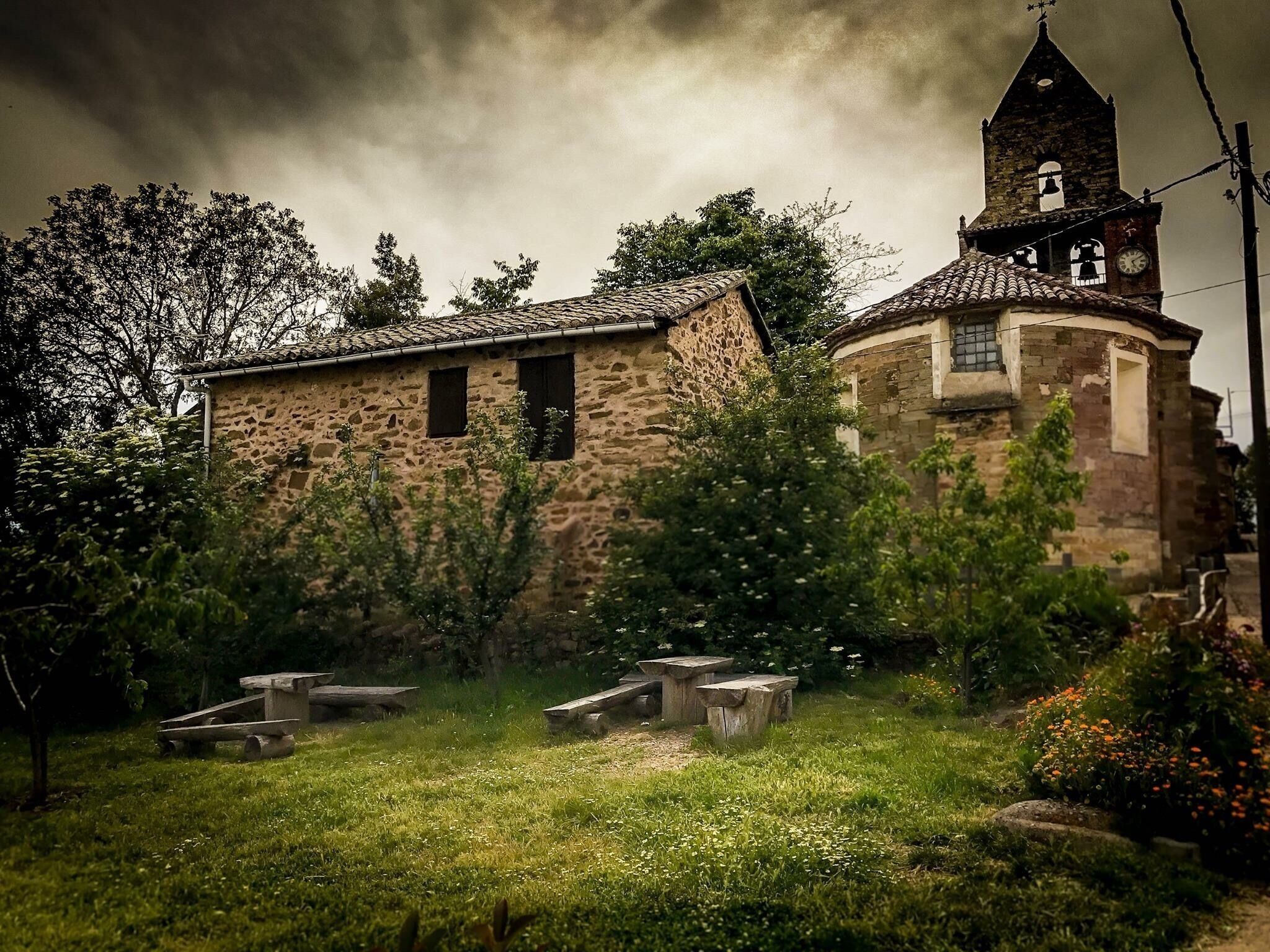 A stone church with a bell tower and a garden with benches.