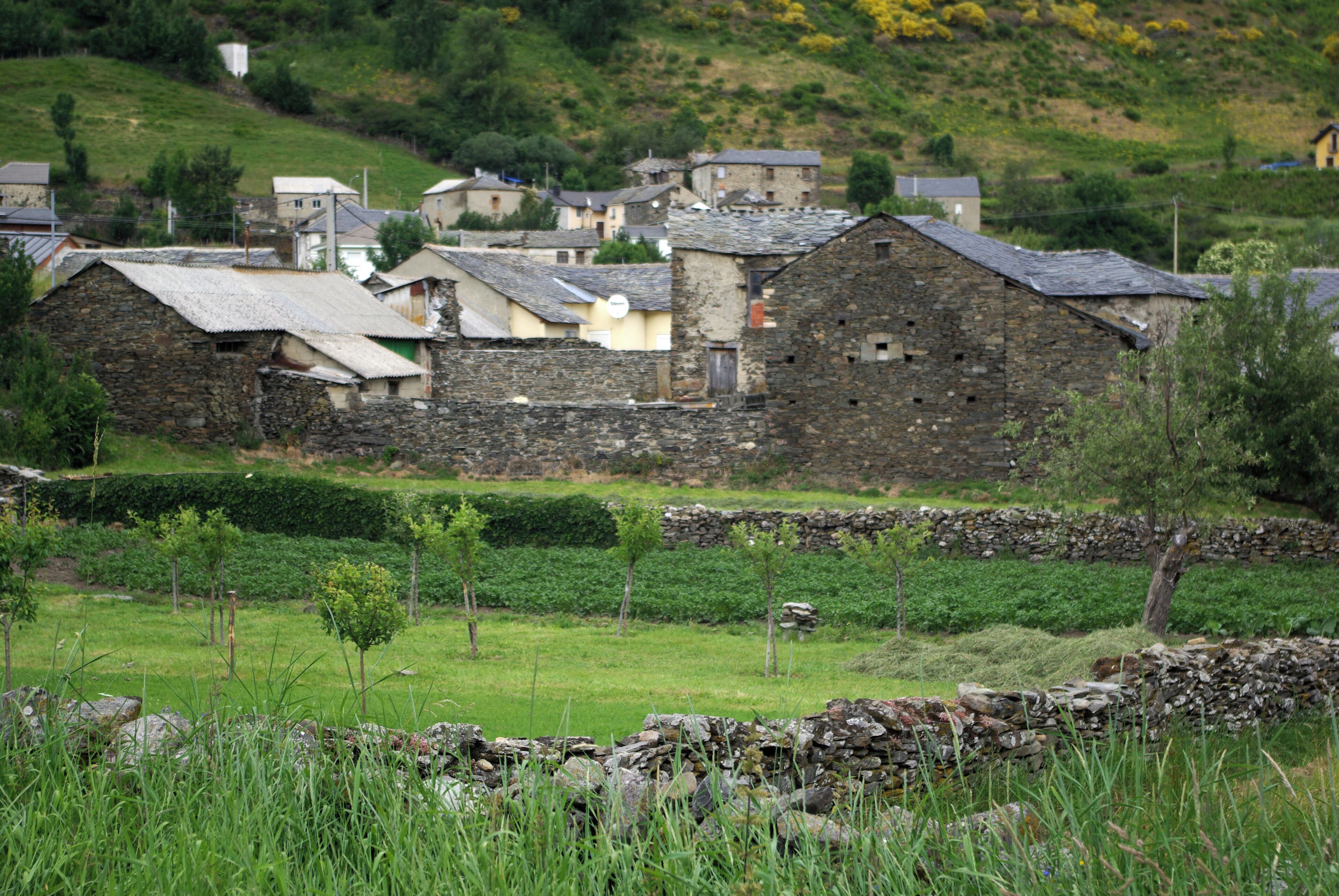 A rural village with stone buildings, green fields, and a hillside in the background.